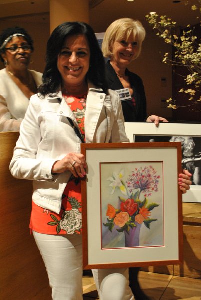 A woman holding up a framed art painting of various flowers in a vase.